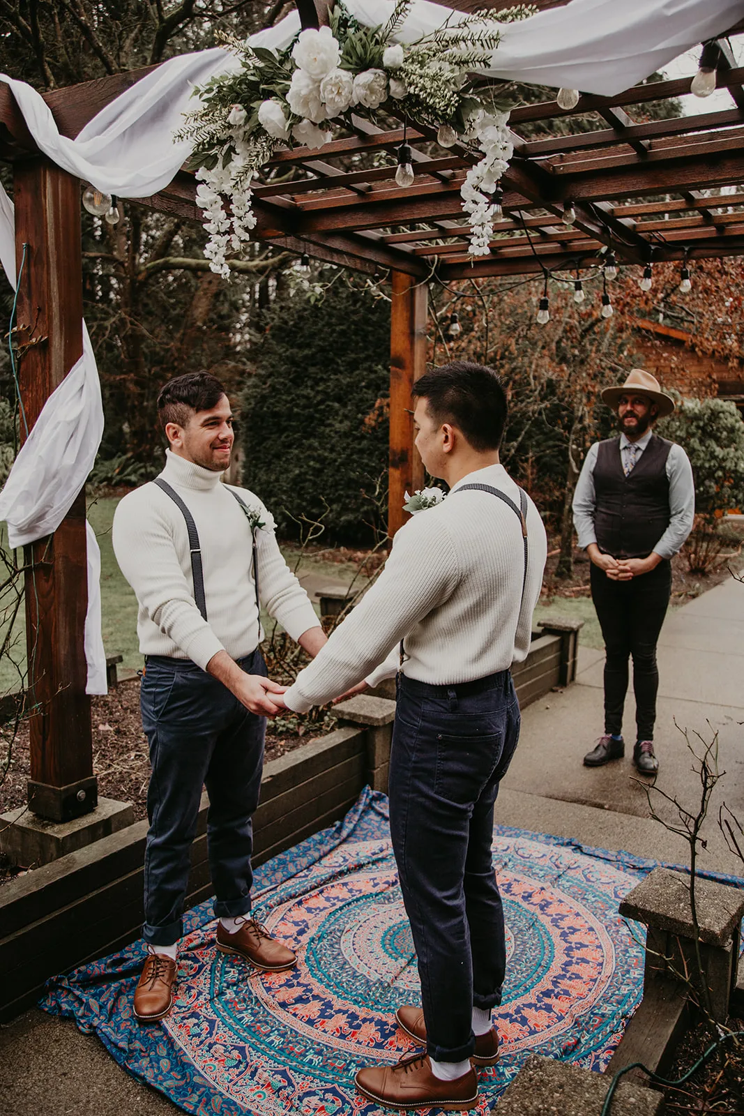 Shawn Miller officiating a ceremony while the two grooms hold hands in front of him