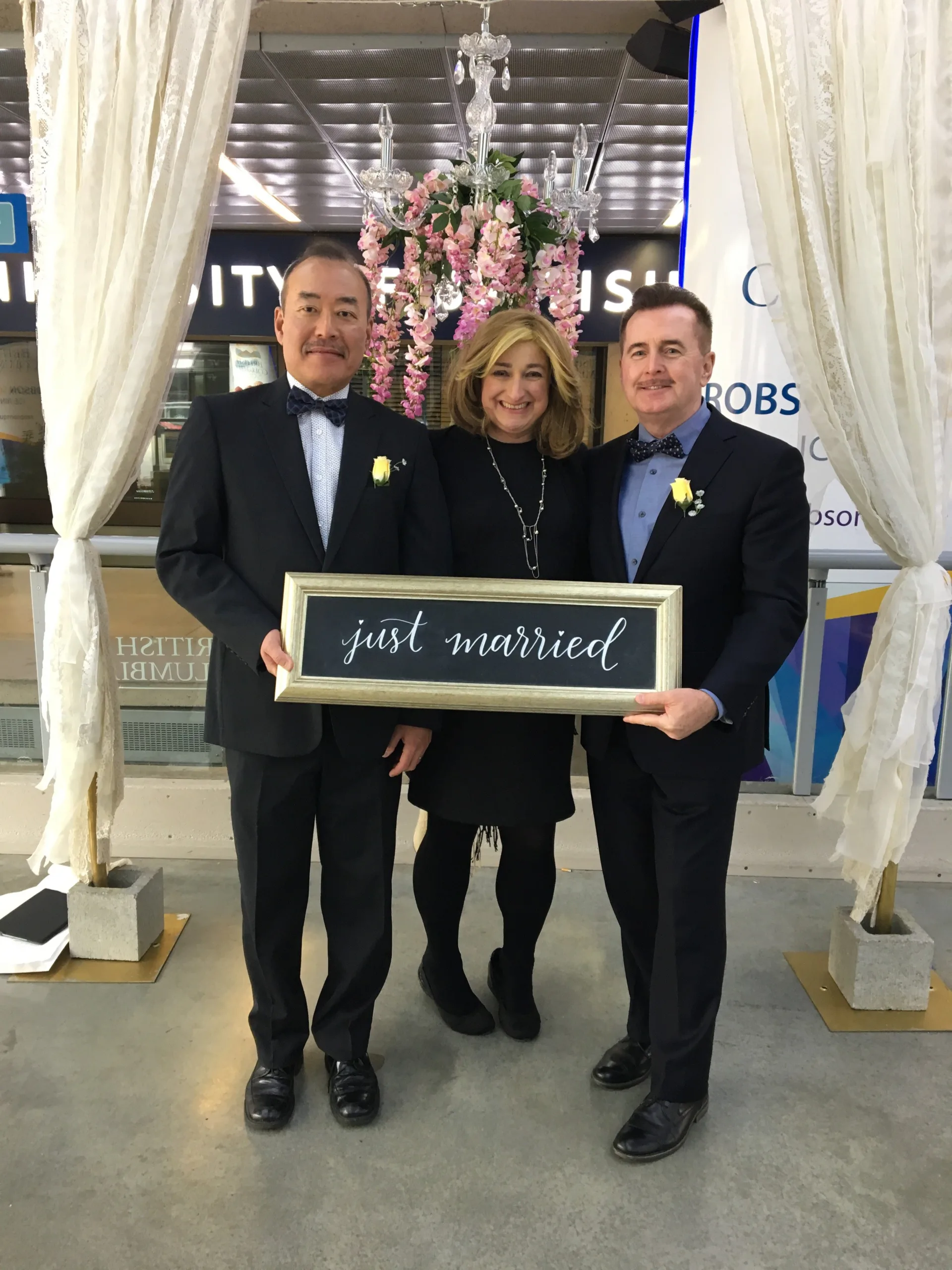 Newlyweds Angus & Daichan pose with Officiant Lauren and a sign that says "just married"