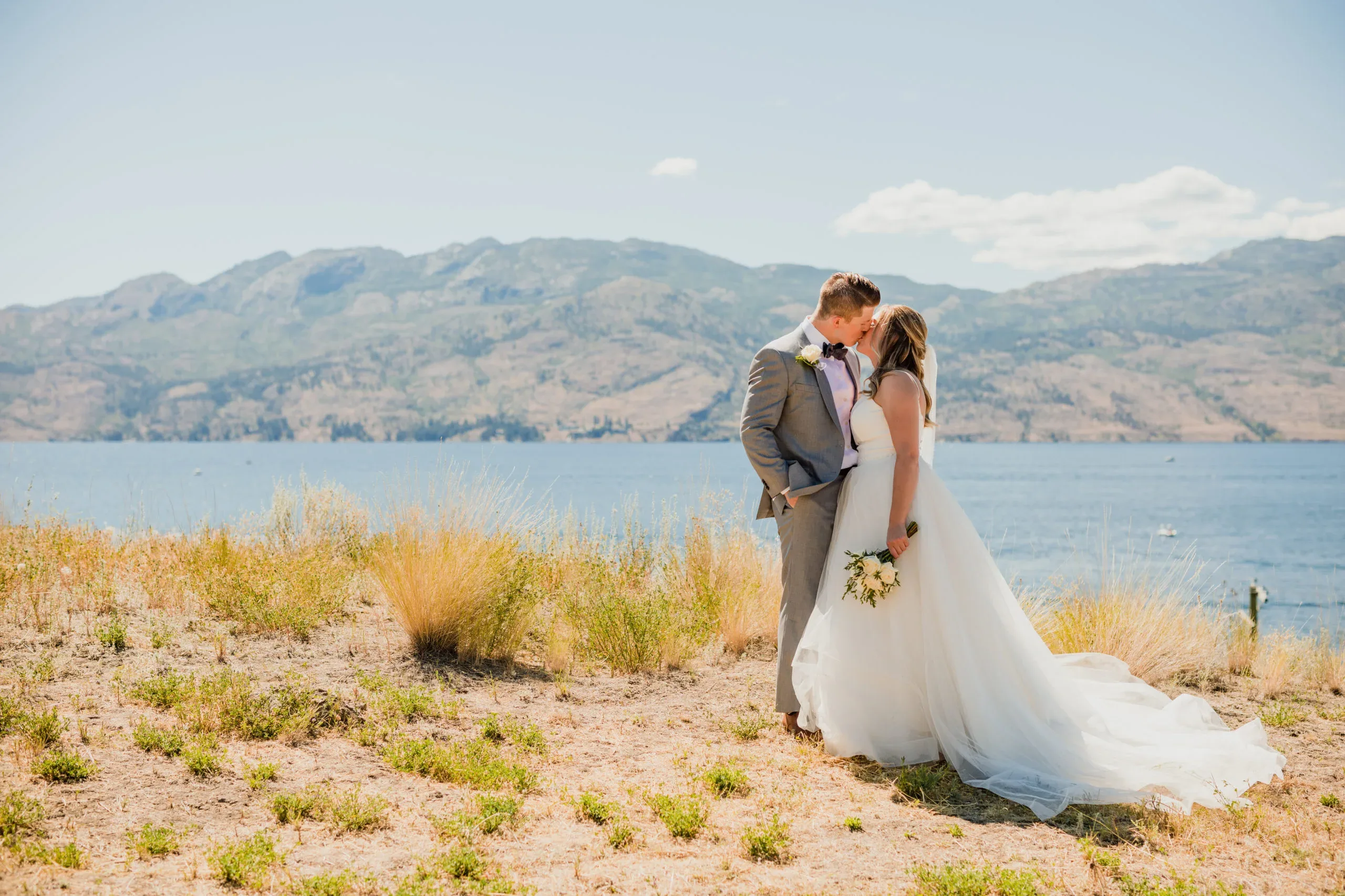 Newlywed couple kissing on a field overlooking Okanagan Lake