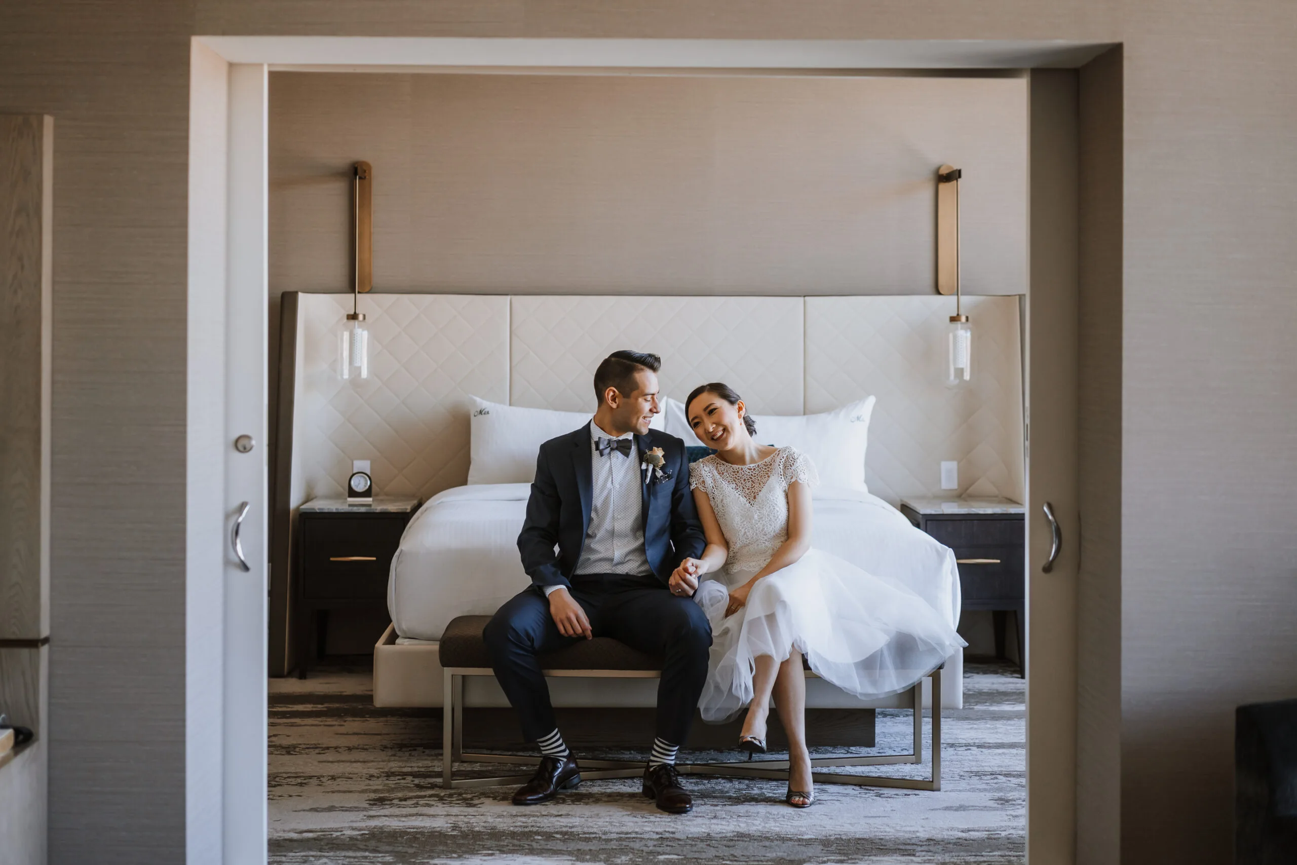 Bride and groom sitting in front of the bed in a suite at the Fairmont Vancouver Airport ahead of their Young Hip & Married elopement