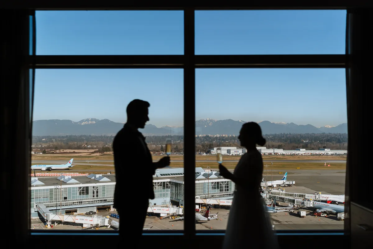 Runway Elopement at the Fairmont Vancouver Airport; silhouette of bride and groom saying their vows in front of a window overlooking the runway