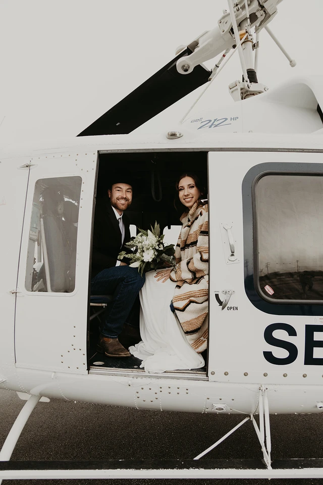 Bride and groom sticking their heads out of a helicopter before their elopement