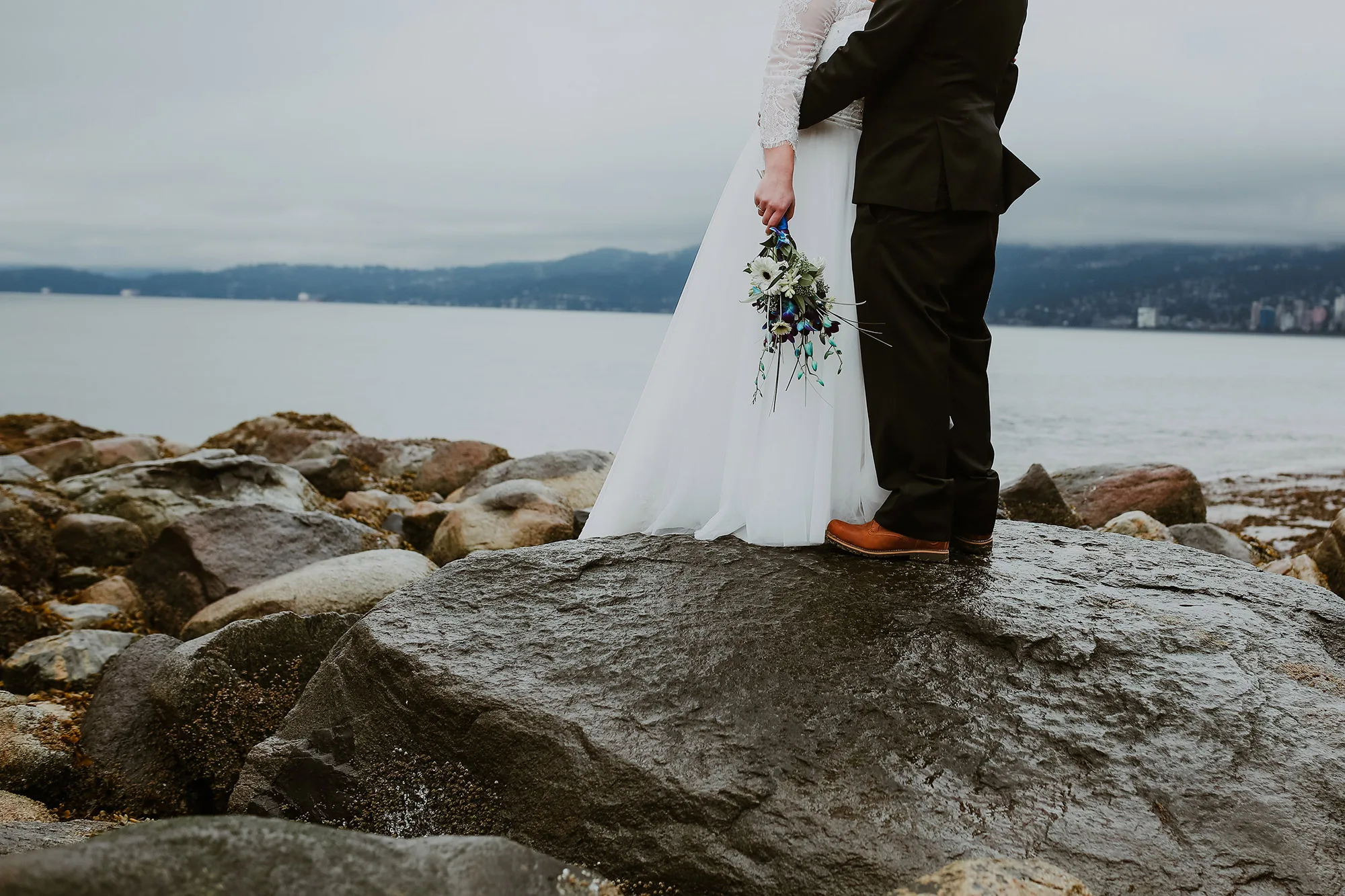 Bride and groom standing on rocks at Stanley Park over the water