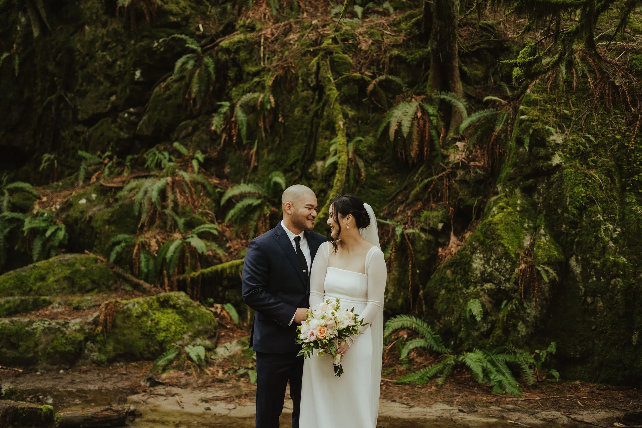 Newlywed couple posing in front of greenery in BC
