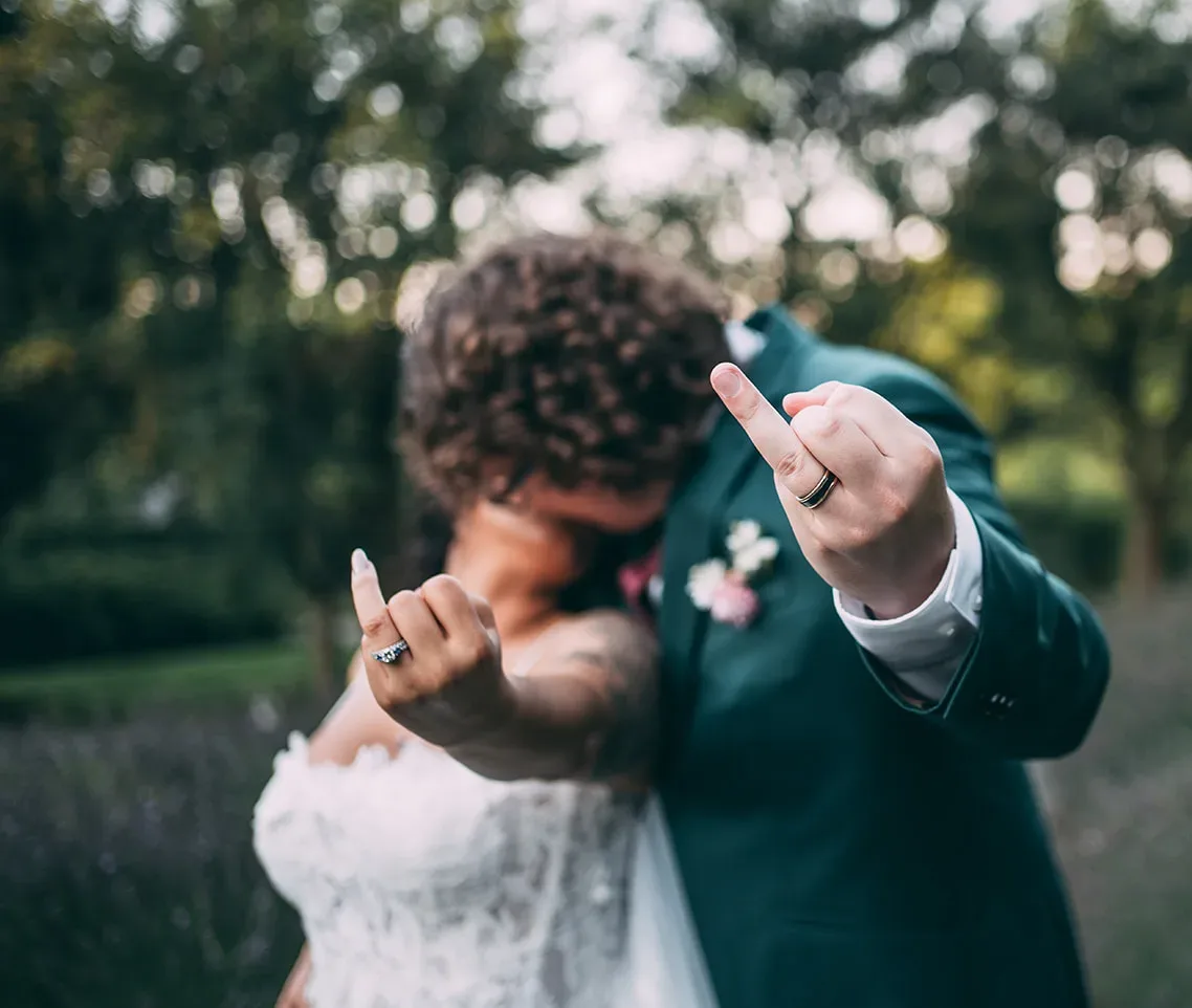 Newlywed couple kissing and holding up their ring fingers to the camera