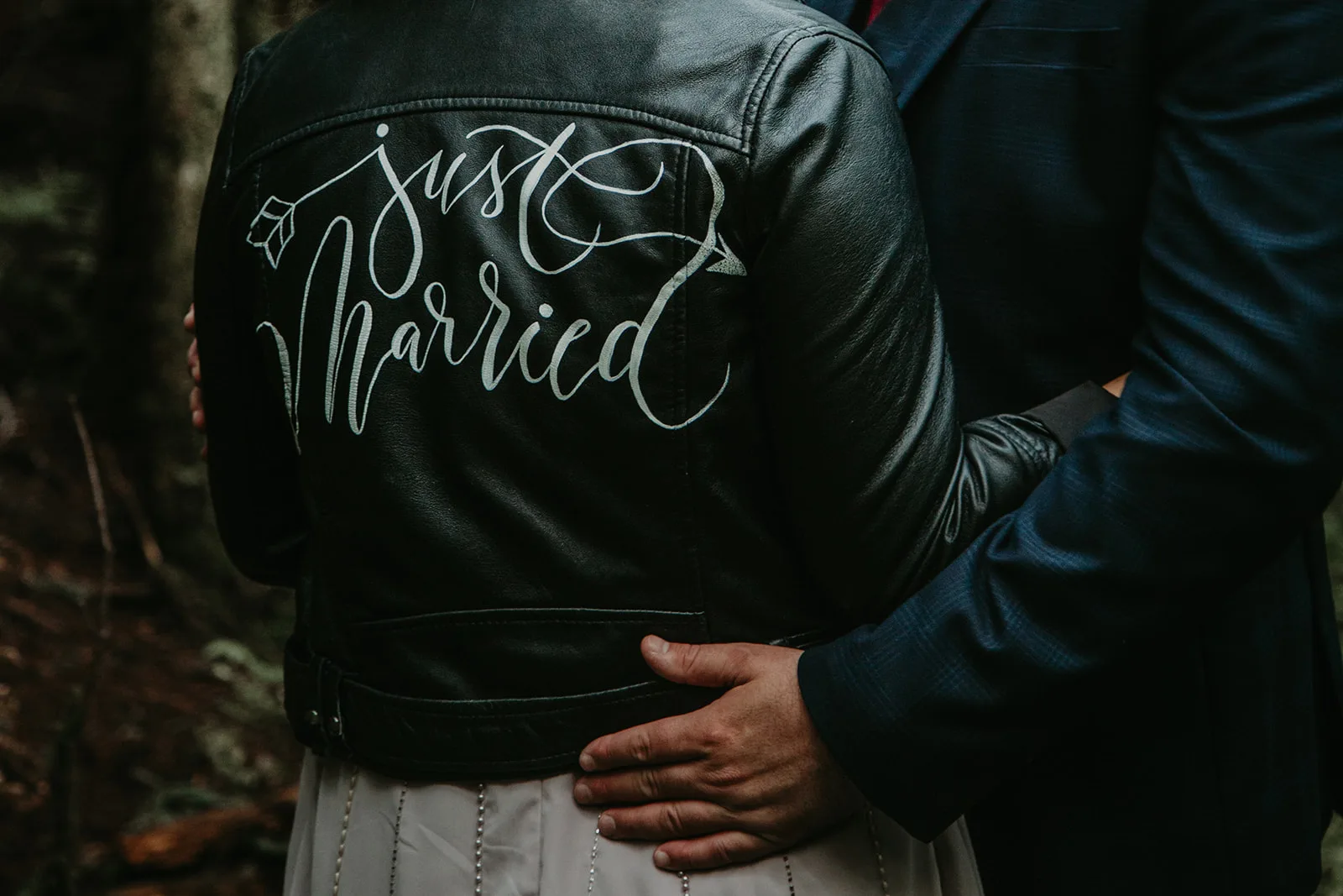 Newlywed couple, bride has her back to the camera showing off a jacket that says "just married"
